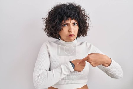 Foto de Hispanic woman with curly hair standing over isolated background in hurry pointing to watch time, impatience, upset and angry for deadline delay - Imagen libre de derechos
