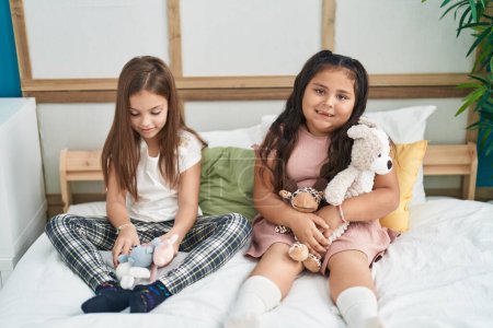 Téléchargez les photos : Two kids playing with dolls sitting on bed at bedroom - en image libre de droit