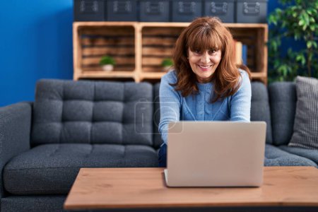 Photo for Middle age woman using laptop sitting on sofa at home - Royalty Free Image