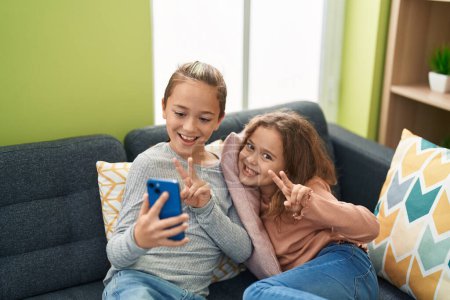 Téléchargez les photos : Deux enfants font selfie par smartphone assis sur le canapé à la maison - en image libre de droit
