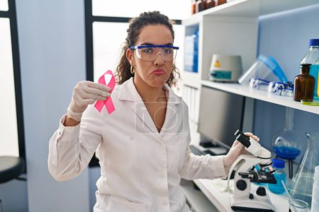 Foto de Young hispanic woman working at scientist laboratory looking for breast cancer cure depressed and worry for distress, crying angry and afraid. sad expression. - Imagen libre de derechos