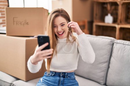 Photo for Young blonde woman holding key make selfie by the smartphone at new home - Royalty Free Image