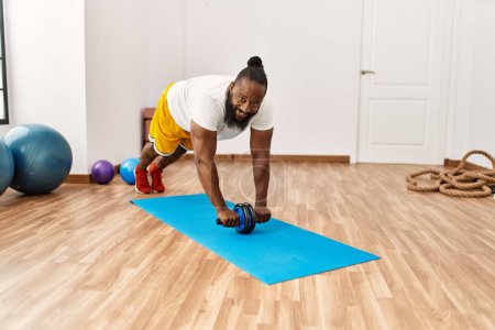 Photo for Young african american man smiling confident training abs exercise using roller at sport center - Royalty Free Image