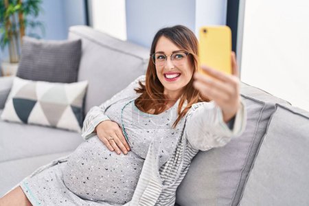 Photo for Young pregnant woman make selfie by smartphone sitting on sofa at home - Royalty Free Image