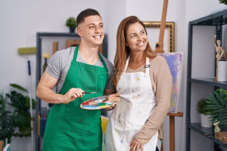 Téléchargez les photos : Man and woman artists smiling confident holding paintbrush and palette at art studio - en image libre de droit