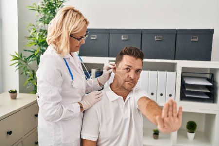 Hombre hispano recibiendo audífono médico en el médico con la mano abierta haciendo señal de stop con expresión seria y segura, gesto de defensa 