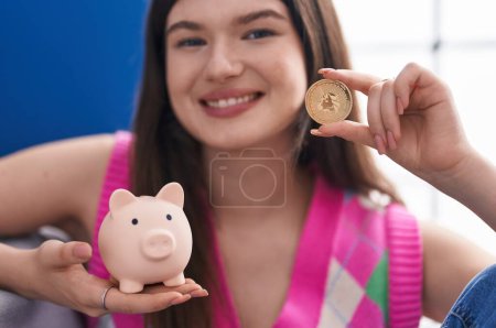 Foto de Joven mujer caucásica sonriendo confiado sosteniendo uniswap moneda y alcancía en casa - Imagen libre de derechos