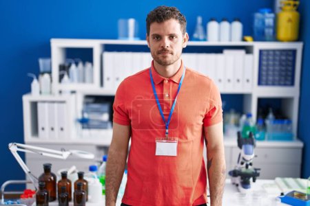 Téléchargez les photos : Young hispanic man working at scientist laboratory relaxed with serious expression on face. simple and natural looking at the camera. - en image libre de droit