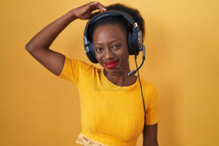 Téléchargez les photos : African woman with curly hair standing over yellow background wearing headphones confuse and wonder about question. uncertain with doubt, thinking with hand on head. pensive concept. - en image libre de droit