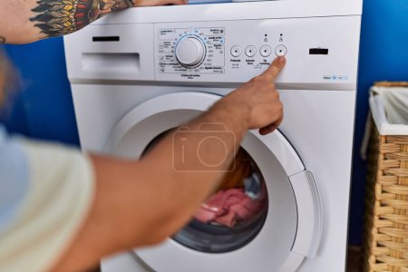 Téléchargez les photos : Jeune rousse homme allumant la machine à laver à la buanderie - en image libre de droit