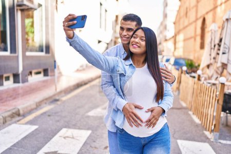 Photo for Young latin couple expecting baby making selfie by the smartphone at street - Royalty Free Image
