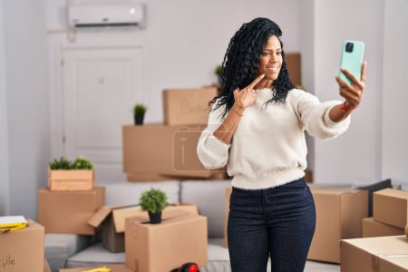 Téléchargez les photos : Middle age hispanic woman moving to a new home taking selfie picture smiling happy pointing with hand and finger - en image libre de droit