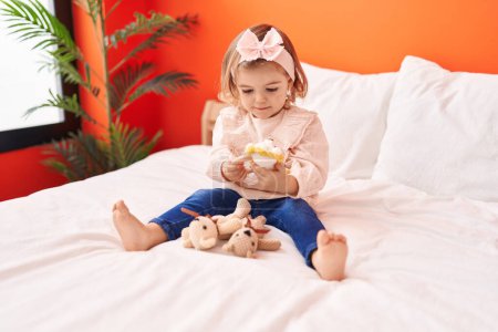 Foto de Adorable niño rubio jugando con juguetes sentados en la cama en el dormitorio - Imagen libre de derechos