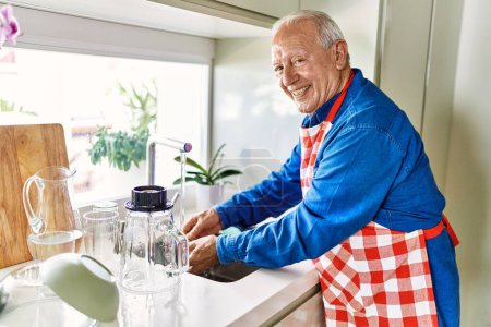 Téléchargez les photos : Senior homme souriant verre de lavage confiant à la cuisine - en image libre de droit