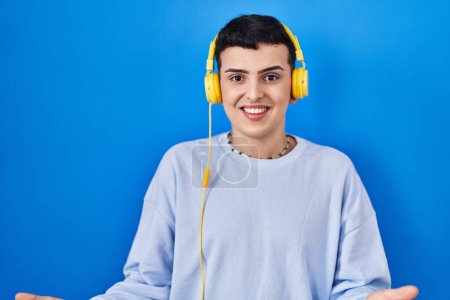 Téléchargez les photos : Non binary person listening to music using headphones smiling cheerful with open arms as friendly welcome, positive and confident greetings - en image libre de droit