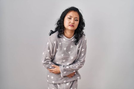 Téléchargez les photos : Young asian woman wearing pajama with hand on stomach because indigestion, painful illness feeling unwell. ache concept. - en image libre de droit