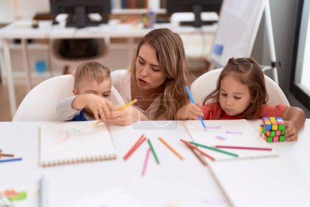 Photo for Teacher with boy and girl sitting on table drawing on paper at kindergarten - Royalty Free Image