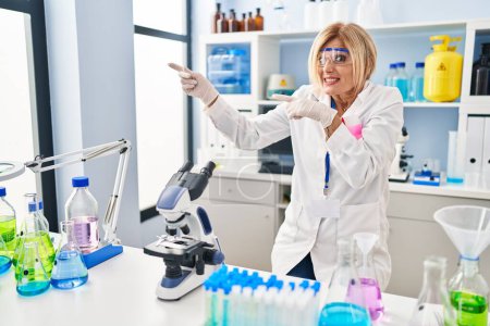 Foto de Middle age blonde woman working at scientist laboratory pointing aside worried and nervous with both hands, concerned and surprised expression - Imagen libre de derechos