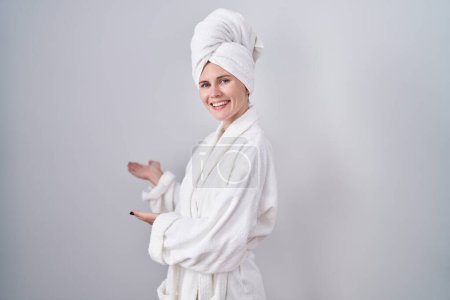 Photo for Blonde caucasian woman wearing bathrobe inviting to enter smiling natural with open hand - Royalty Free Image