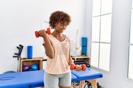 Photo for Young african american woman doing rehab using dumbbells at clinic - Royalty Free Image