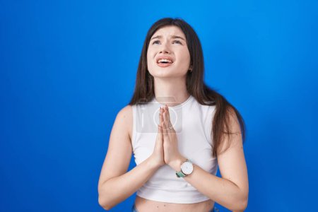 Photo for Young caucasian woman standing over blue background begging and praying with hands together with hope expression on face very emotional and worried. begging. - Royalty Free Image