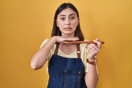 Photo for Hispanic girl eating healthy  wooden spoon cutting throat with hand as knife, threaten aggression with furious violence - Royalty Free Image