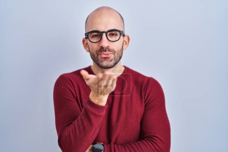 Foto de Young bald man with beard standing over white background wearing glasses looking at the camera blowing a kiss with hand on air being lovely and sexy. love expression. - Imagen libre de derechos