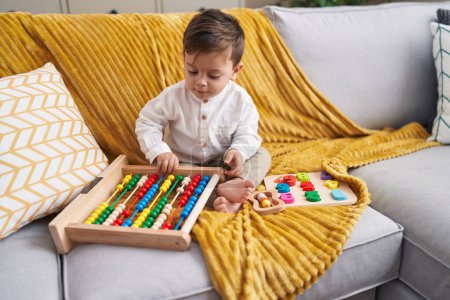 Foto de Adorable hispanic boy playing with abacus sitting on sofa at home - Imagen libre de derechos