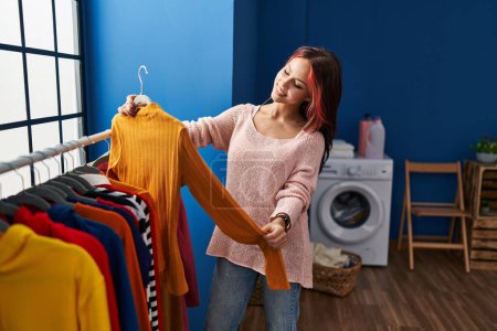 Photo for Young caucasian woman holding sweatshirt on rack at laundry room - Royalty Free Image