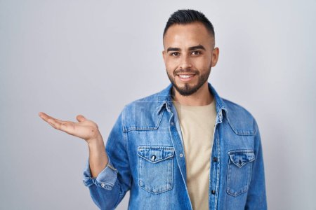 Téléchargez les photos : Jeune homme hispanique debout sur fond isolé souriant gai présentation et pointant avec la paume de la main en regardant la caméra. - en image libre de droit