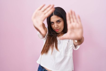 Foto de Young arab woman standing over pink background doing frame using hands palms and fingers, camera perspective - Imagen libre de derechos