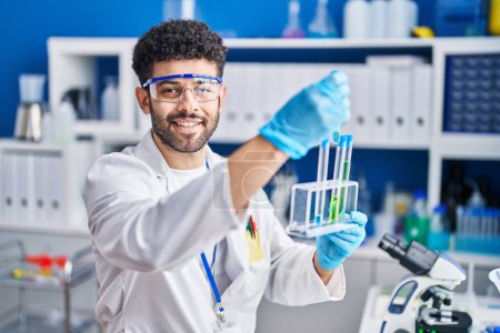 Téléchargez les photos : Jeune homme arabe portant l'uniforme scientifique tenant des éprouvettes au laboratoire - en image libre de droit