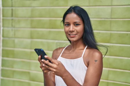Foto de Joven hermosa mujer sonriendo confiado usando teléfono inteligente sobre fondo verde aislado - Imagen libre de derechos