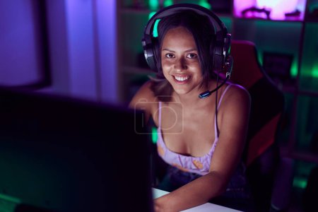 Foto de Mujer hispana joven streamer sonriendo confiado jugando videojuego en la sala de juegos - Imagen libre de derechos