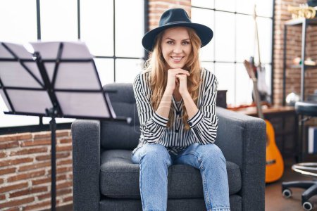 Téléchargez les photos : Young blonde woman musician smiling confident sitting on sofa at music studio - en image libre de droit