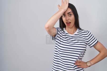 Téléchargez les photos : Jeune femme brune portant t-shirt rayé surpris avec la main sur la tête pour erreur, rappelez-vous erreur. oublié, mauvais concept de mémoire. - en image libre de droit