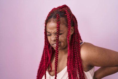 Téléchargez les photos : African american woman with braided hair standing over pink background suffering of backache, touching back with hand, muscular pain - en image libre de droit