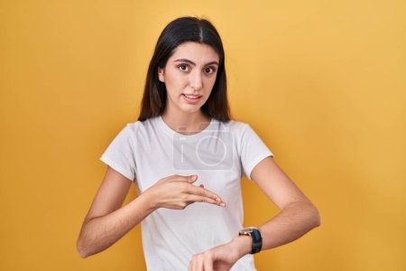 Téléchargez les photos : Young beautiful woman standing over yellow background in hurry pointing to watch time, impatience, upset and angry for deadline delay - en image libre de droit