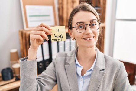 Foto de Young caucasian woman business worker holding sticker with smiling and thanks message at office - Imagen libre de derechos
