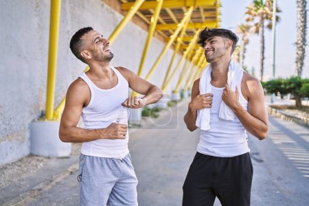 Téléchargez les photos : Deux hommes hispaniques couple sportif souriant confiant debout dans la rue - en image libre de droit