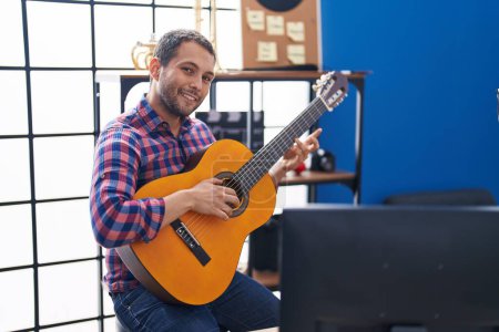 Foto de Joven músico sonriendo confiado tocando la guitarra clásica en el estudio de música - Imagen libre de derechos
