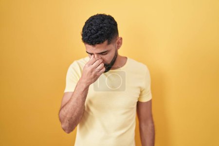 Foto de Hispanic man with beard standing over yellow background tired rubbing nose and eyes feeling fatigue and headache. stress and frustration concept. - Imagen libre de derechos