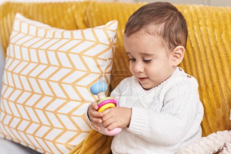 Foto de Adorable niño hispano jugando con un juguete sentado en un sofá en casa - Imagen libre de derechos