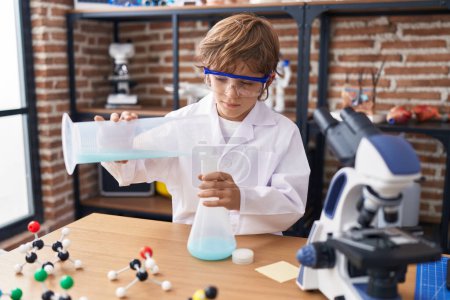 Foto de Adorable caucásico chico estudiante verter líquido en tubo de ensayo en el aula - Imagen libre de derechos