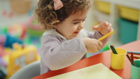 Foto de Adorable hispanic girl preschool student sitting on table drawing on paper at kindergarten - Imagen libre de derechos