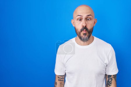 Photo for Hispanic man with tattoos standing over blue background making fish face with lips, crazy and comical gesture. funny expression. - Royalty Free Image