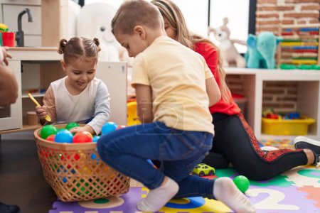 Foto de Profesor con niño y niña jugando con bolas sentados en el suelo en el jardín de infantes - Imagen libre de derechos