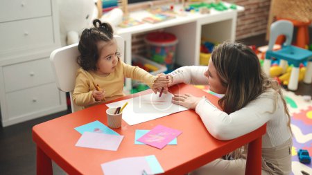 Téléchargez les photos : Teacher and toddler sitting on table drawing on paper at kindergarten - en image libre de droit