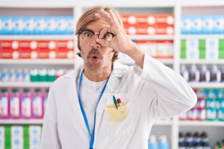 Téléchargez les photos : Homme caucasien avec moustache travaillant à la pharmacie pharmacie faisant un geste correct choqué par le visage surpris, les yeux regardant à travers les doigts. expression incrédule. - en image libre de droit