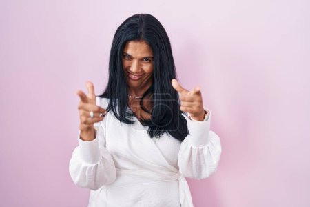 Téléchargez les photos : Femme hispanique mature debout sur fond rose pointant les doigts vers la caméra avec un visage heureux et drôle. bonne énergie et vibes. - en image libre de droit